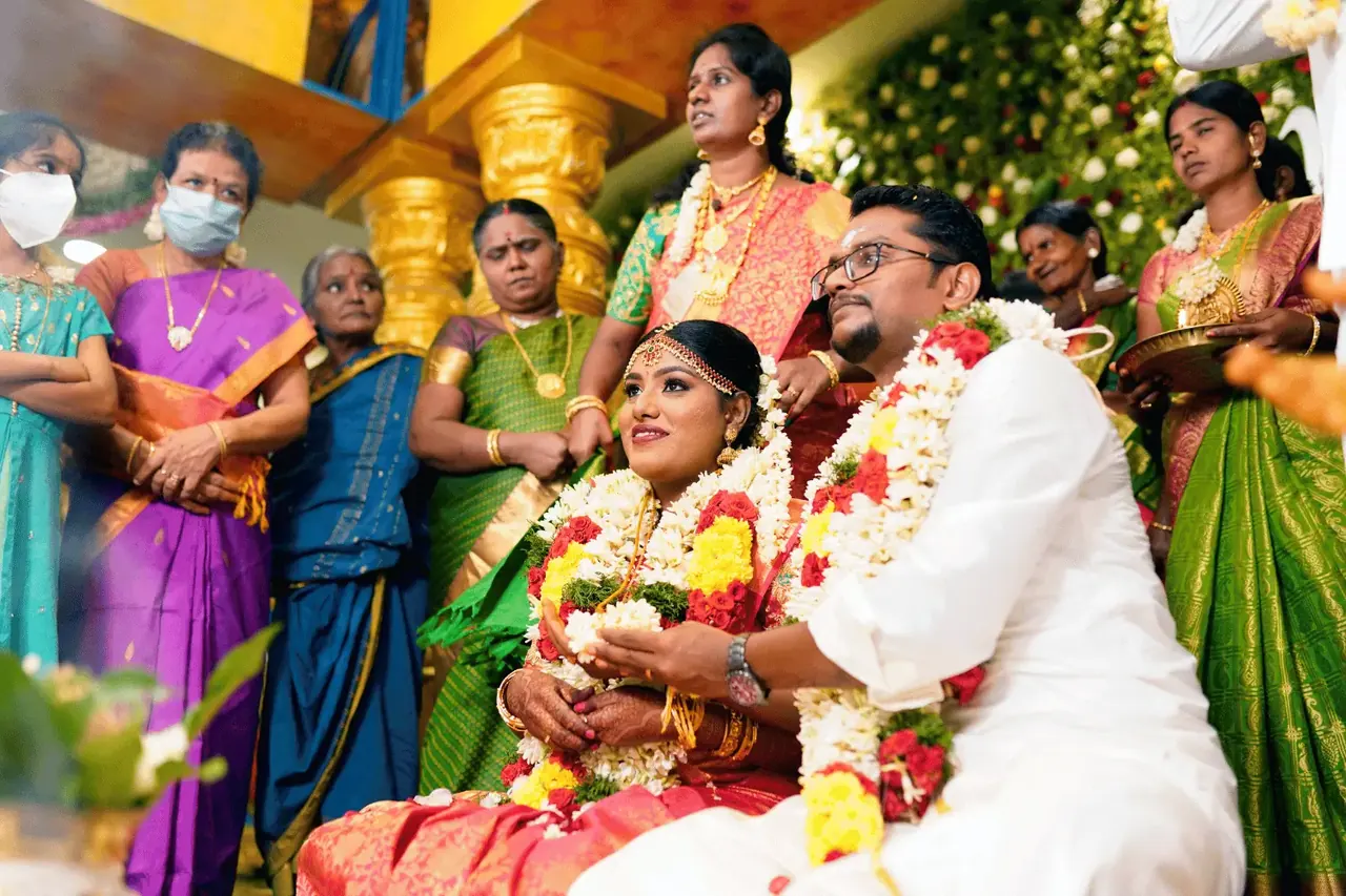 Bride and groom in wedding garlands seated with family during a traditional wedding ceremony